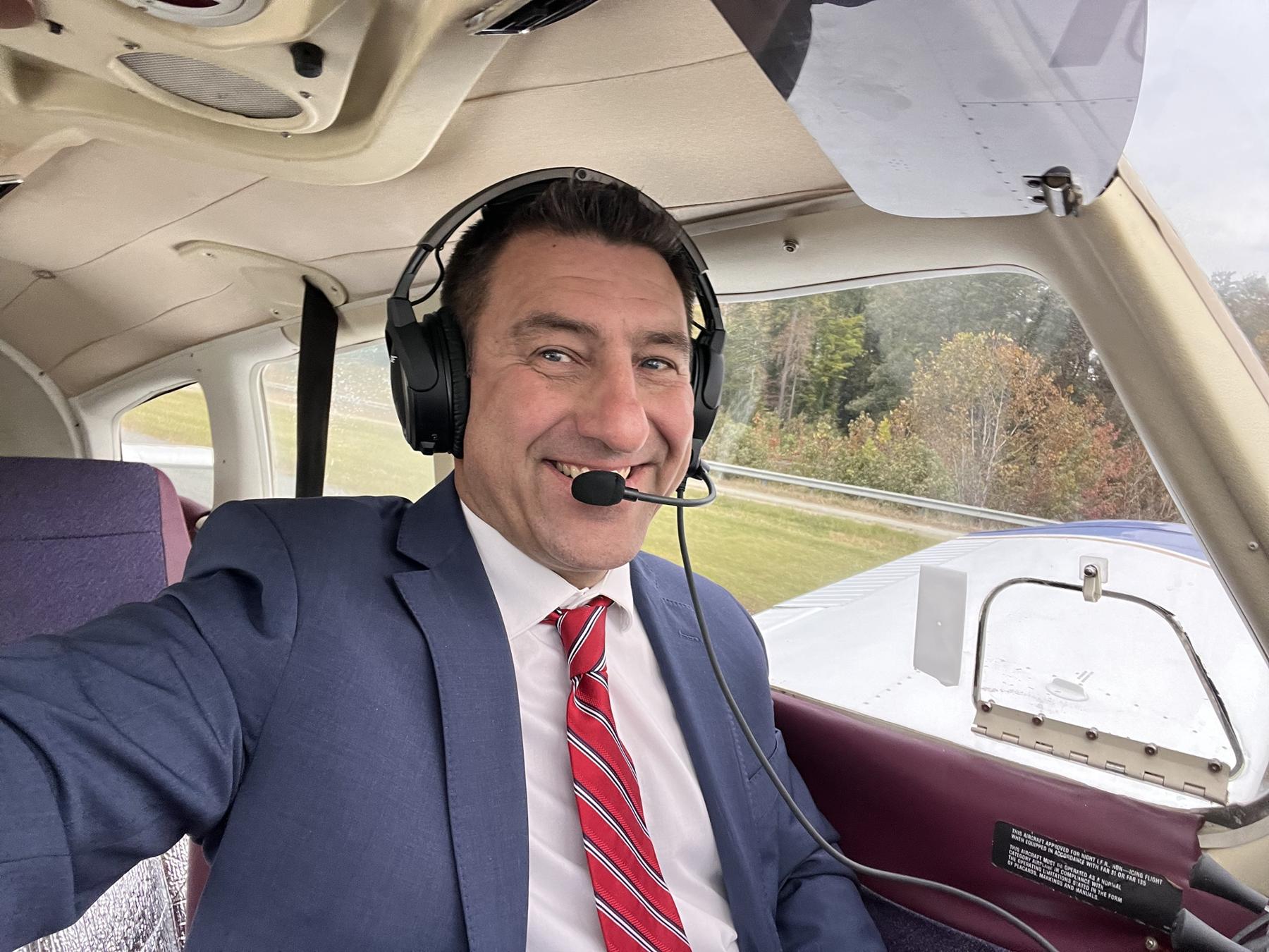 Julian Doby in a navy suit and headset in the left seat, the wing visible through the window