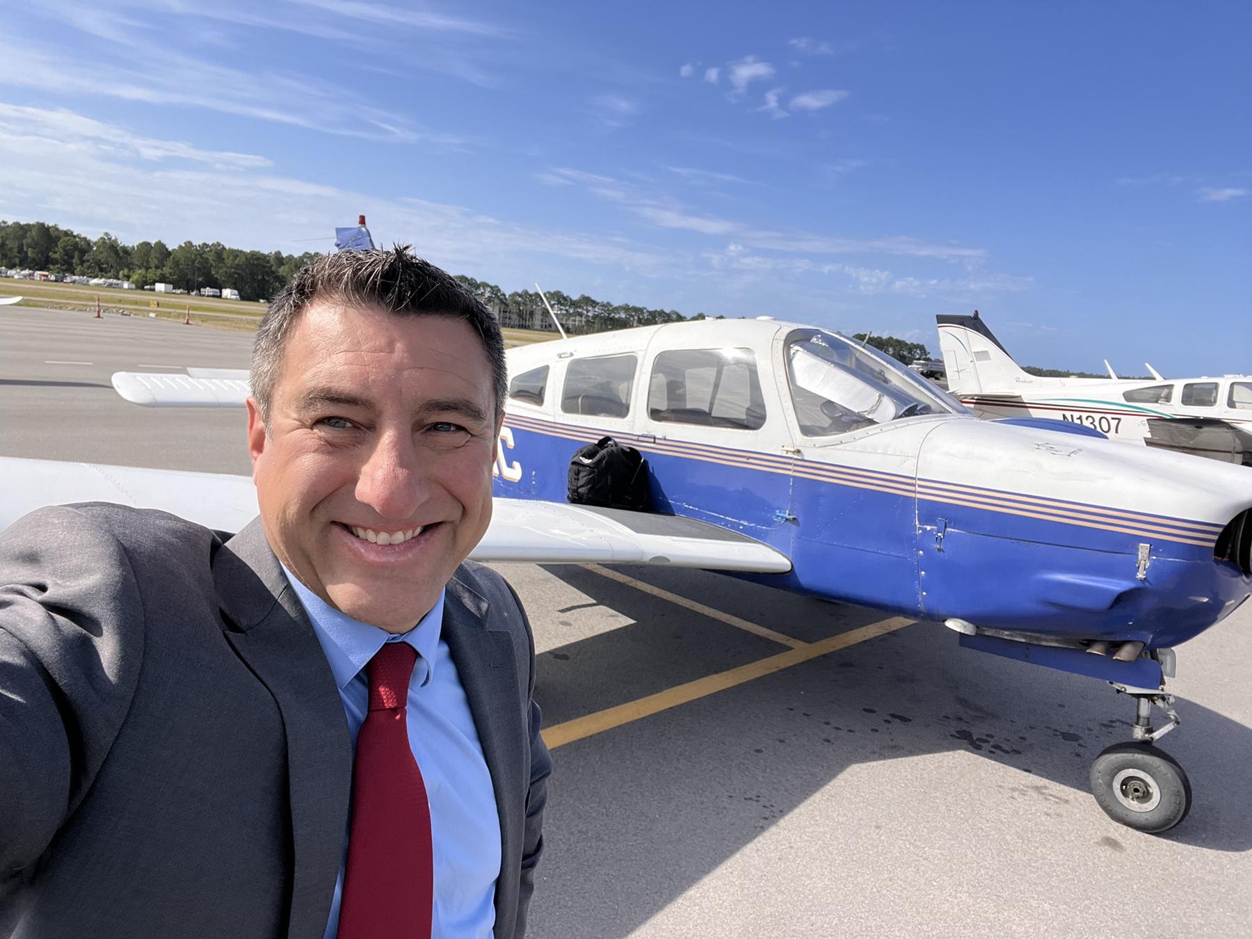 Julian Doby in a suit beside his blue and white Piper on an airport ramp