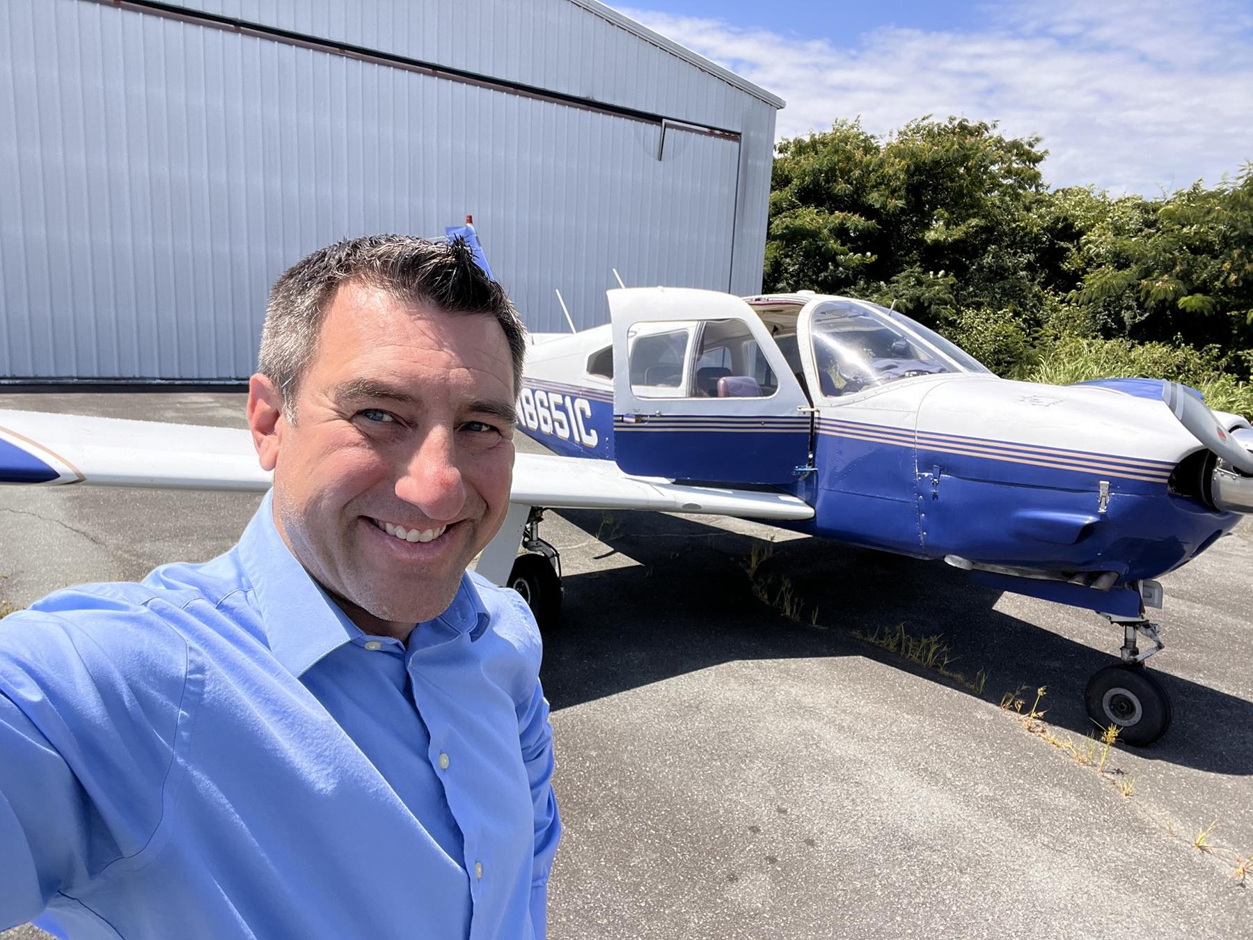 The blue and white Piper parked beside its hangar with the cabin door open